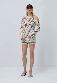Set in maglia leggera composto da una maglietta a maniche lunghe con spalle scoperte e pantaloni corti in crema con motivi geometrici neri e marroni.