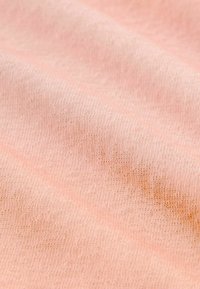 Tissu pêche avec un tissage fin et texturé ; présente des plis doux et un léger éclat. La surface semble lisse avec des variations de couleur subtiles.
