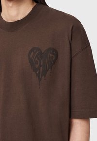 Brun bomulds-T-shirt med et stort sort hjerte med dryppende elementer. Korte ærmer og rund halsudskæring. Simpelt, afslappet design.