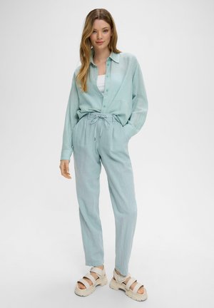Light blue, long-sleeve, button-up shirt paired with matching, drawstring trousers and beige platform sandals. Soft, textured fabric.