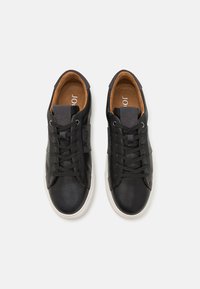 Sorte lær sneakers med rund tå, kremfarget gummisåle og snørelukking. Har en grå tekstilaccent på siden og en brun innside.