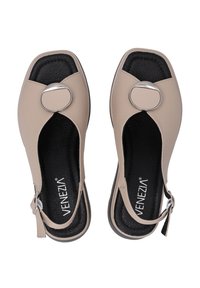 Beige open-toe schoenen met een ronde metalen accent, een verstelbare band en een gestructureerde zwarte binnenzool. Platte zool met minimale profiel.