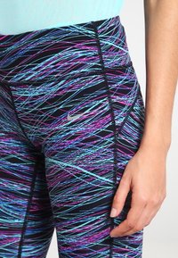 Leggings noirs taille haute avec un motif abstrait de lignes bleues, roses et violettes ; comporte un logo Nike argenté et des coutures renforcées.