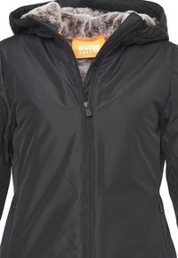 Giacca nera con zip e cappuccio, dotata di una morbida fodera in pelliccia grigia e un'etichetta arancione. Progettata con dettagli delle cuciture e tasche laterali.