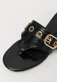 Sandalo in pelle nera con una texture liscia, dotato di una fascia larga con occhielli in metallo dorato e un elegante cinturino decorativo in oro.