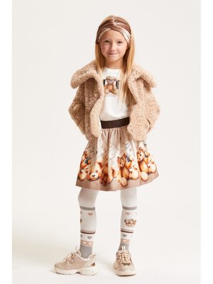 Veste en fausse fourrure beige, t-shirt blanc avec un graphique d'ours, jupe beige à imprimé animal, collants gris à motifs et baskets beiges.