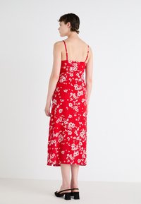 Rød blomstrete midi-kjole med tynne stropper, en tettsittende bodice og en flytende hem. Har hvite blomsterprint og svarte blokkhæl sandaler.