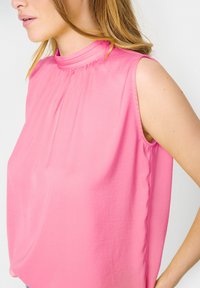 Top senza maniche rosa con colletto alto, dettagli plissettati, texture liscia e vestibilità comoda, presentato su uno sfondo neutro.