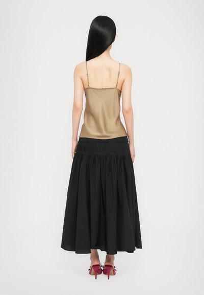 Tan satin camisole with thin straps, paired with a black, pleated long skirt. Red heels with bows detail complete the ensemble.