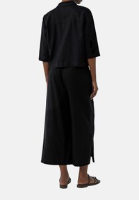 Set di due pezzi in lino nero composto da una camicia corta con bottoni e pantaloni a gamba larga. Texture liscia con design minimalista e senza motivi visibili.
