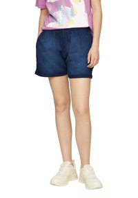 Shorts en mélange de lin bleu marine avec une taille élastique, présentant une coupe décontractée et un ourlet roulé. Associés à un t-shirt graphique rose et des baskets blanches.