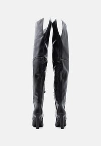 Botas de cuero negras por encima de la rodilla con una textura suave, altos tacones de aguja y un diseño único de apertura en la parte superior. Cierres con cremallera a los lados.