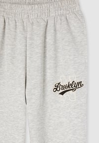 Szare dresy z elastycznym paskiem w talii, z czarno-kremowym nadrukiem logo "Brooklyn" oraz obrysowaną literą "N" na nogawce.
