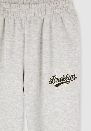 Pantaloni della tuta grigi con cintura elastica, caratterizzati da un logo "Brooklyn" stampato in nero e crema e da una lettera "N" delineata sulla gamba.