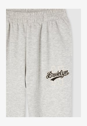 Pantaloni della tuta grigi con cintura elastica, caratterizzati da un logo "Brooklyn" stampato in nero e crema e da una lettera "N" delineata sulla gamba.