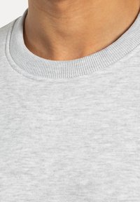 Grå sweatshirtstof med ribbet rund hals, der har en blød tekstur og et subtilt meleret mønster. Nærbillede af halsområdet.