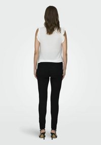 Haut blanc à manches courtes avec un motif texturé, associé à un jean skinny noir et des talons verts, vu de dos.