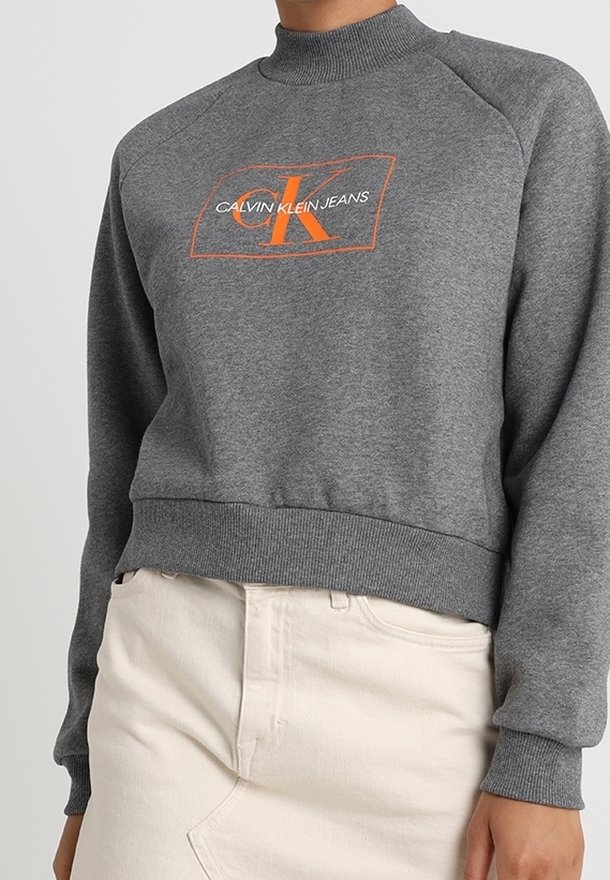 Felpa grigia con collo alto e maniche raglan, caratterizzata da un logo arancione "CK" e testo, realizzata in morbido tessuto di cotone.