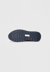 Rubberen sneakersole, marineblauw, met textuur en diepe groeven voor grip. Inclusief een witte rechthoekige acccent nabij de tussenzool.