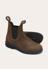 Botas de tobillo de cuero marrón con paneles laterales elásticos, tiradores y suelas de goma negra texturizada. Superficie lisa y duradera con un diseño clásico.