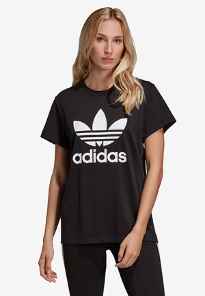 Zwarte katoenen t-shirt met een groot wit Adidas-logo met drie blaadjes ontwerp op de borst. Korte mouwen en een ronde halslijn.
