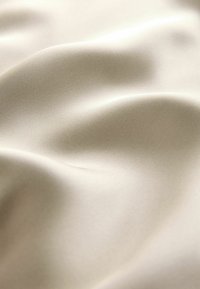 Béžová saténová látka s hladkou textúrou, ktorá zobrazuje jemné záhyby a subtílny lesk, zdôrazňujúca jej schopnosť splývať a strednú hmotnosť.