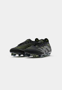 Black football cleats with textured upper, green accents, and a sleek design. Equipped with transparent studs for traction on the field.