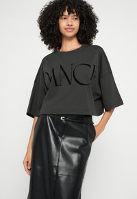 Tmavě šedé krátké tričko s výrazně oversize rukávy a lesklým nápisem "DANCE". Kombinováno s černou koženou sukní a úzkým opaskem.