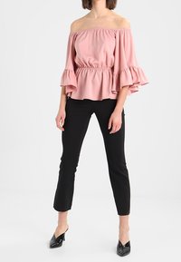 Haut rose à épaules dénudées avec des manches volantes et taille élastique. Associé à un pantalon noir ajusté et des escarpins noirs à talons pointus.