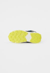 Semelle d'une chaussure de sport noire avec un motif de bande de roulement en caoutchouc jaune texturé et une semelle intermédiaire blanche. Présente un accent de marque.