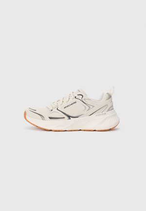 Beige athletic shoe with a breathable mesh upper, black accents, and a textured rubber sole. Features a cushioned heel and lacing system.