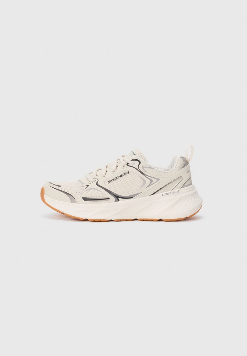Shoe esportivo bege com um cabedal em malha respirável, detalhes em preto e uma sola de borracha texturizada. Apresenta um calcanhar acolchoado e um sistema de atacadores.