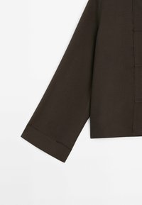 Haut à manches longues de couleur marron foncé avec une coupe droite, doté d'un revers plié et d'une texture lisse. Design simple sans fermetures visibles.