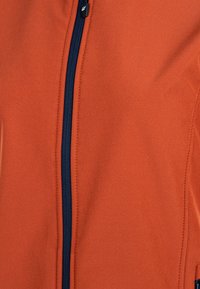 Orange fleecejacka med en marinblå dragkedja, med en slät textur och en figurnära passform. Stygn detaljer längs sömmarna är synliga.