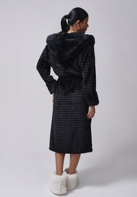 Sort hættebadekåbe med mønstret tekstur, lange ærmer og bindebånd; kombineret med bløde, hvide plyssede tøfler.