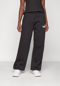 Black sweatpants with a relaxed fit and elastic waistband. Features a logo print on the upper thigh. Material appears soft and textured.