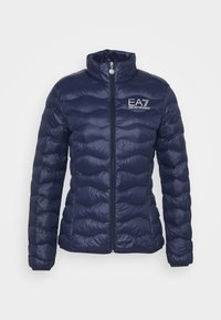 Marinfärgad pufferjacka med dragkedja, hög krage och horisontellt quiltat mönster. Har EA7-logotypen på vänster bröst och en slät, glänsande yta.