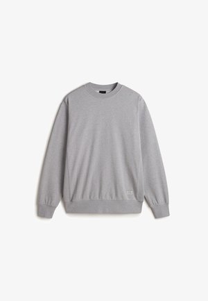 Sweatshirt gris à col rond fabriqué en mélange de coton doux. Il possède des poignets et un ourlet en côte, avec un petit détail d'étiquette sur le bas gauche à l'avant.