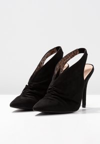 Scarpe slingback nere in suede con tacco alto, punta affusolata e design arricciato nella parte anteriore; l'interno presenta un motivo leopardato.