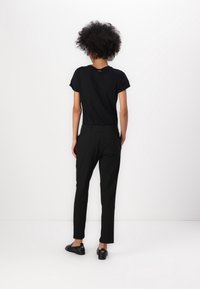 Zwarte T-shirt met korte mouwen, nauwsluitend ontwerp, gecombineerd met zwarte taps toelopende broek en platte schoenen. Gladde textuur, minimale details.