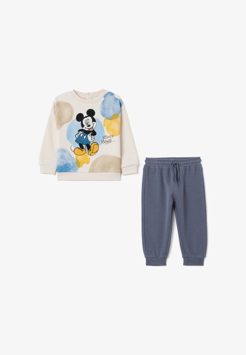 Mickey Mouse sweatshirt in crèmekleur met blauwe en gele patronen, gecombineerd met donkerblauwe sweatpants. Beide gemaakt van zachte, comfortabele stof.