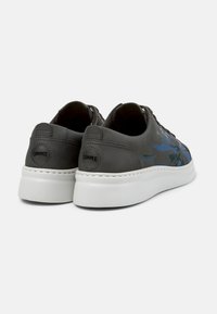 Graue Ledersneaker mit einer weißen Sohle, die blaue und grüne abstrakte Muster, tonale Nähte und ein rundes schwarzes Logo an der Ferse aufweisen.