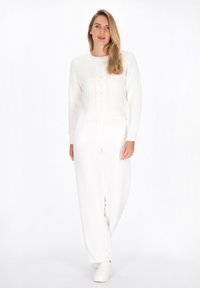 Witte gebreide trui met kabelpatroon, gecombineerd met witte wijde broek en witte sneakers. Zachte textuur en relaxte pasvorm.