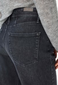 Jean en denim noir avec une texture lisse. Comprend une taille mi-haute, des poches arrière et des détails de couture minimalistes.