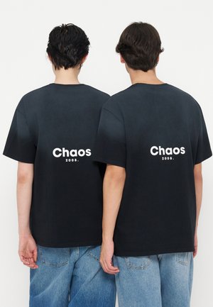 Deux personnes portant des t-shirts noirs avec les mots "Chaos" et "2008" imprimés dans le dos, assortis à un jean bleu.
