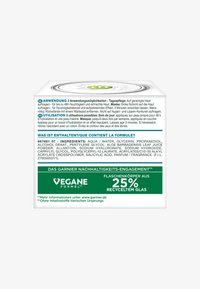 Kwadratowy biały pojemnik o gładkiej powierzchni, z zielonymi akcentami i szczegółowymi informacjami o produkcie w wielu językach na boku.