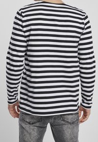 Camicia a maniche lunghe con righe orizzontali alternate nere e bianche, realizzata in tessuto morbido, con collo a giro e vestibilità rilassata.