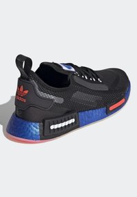 Svart Adidas-sneaker med stickad ovandel, blå strukturerad mellansula, röda accenter, svarta snören och Adidas-logotyp i rött på hälfliken.