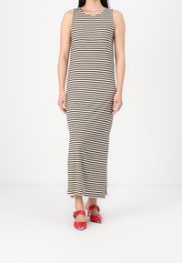 Robe maxi rayée crème et noire, sans manches avec un col rond ; associée à des chaussures à talons rouges à bout pointu.