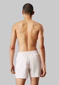 Shorts de bain pour homme en beige clair, dotés d'une taille élastique et d'une poche arrière unique. Tissu lisse et léger avec une coupe décontractée.